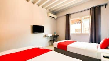 Une chambre d’hôtel avec deux lits, un bureau, une télévision et une fenêtre avec des rideaux.