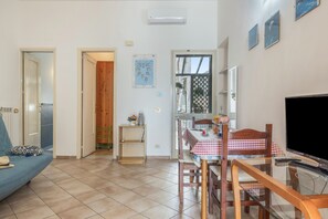 A living room with a sofa, a dining table with chairs, a TV, and a kitchen area with a fridge. - Mondello Holidays - Casa Goethe Apartment with Sea View, WiFi, and Air Conditioning (Palermo)