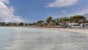 Ein Strand mit klarem Wasser, Sonnenschirmen und Gebäuden im Hintergrund.