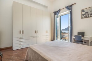 A bedroom with a bed, a desk with a chair, a wardrobe, and a balcony with a view. - Mondello Holidays - Casa Goethe Apartment with Sea View, WiFi, and Air Conditioning (Palermo)