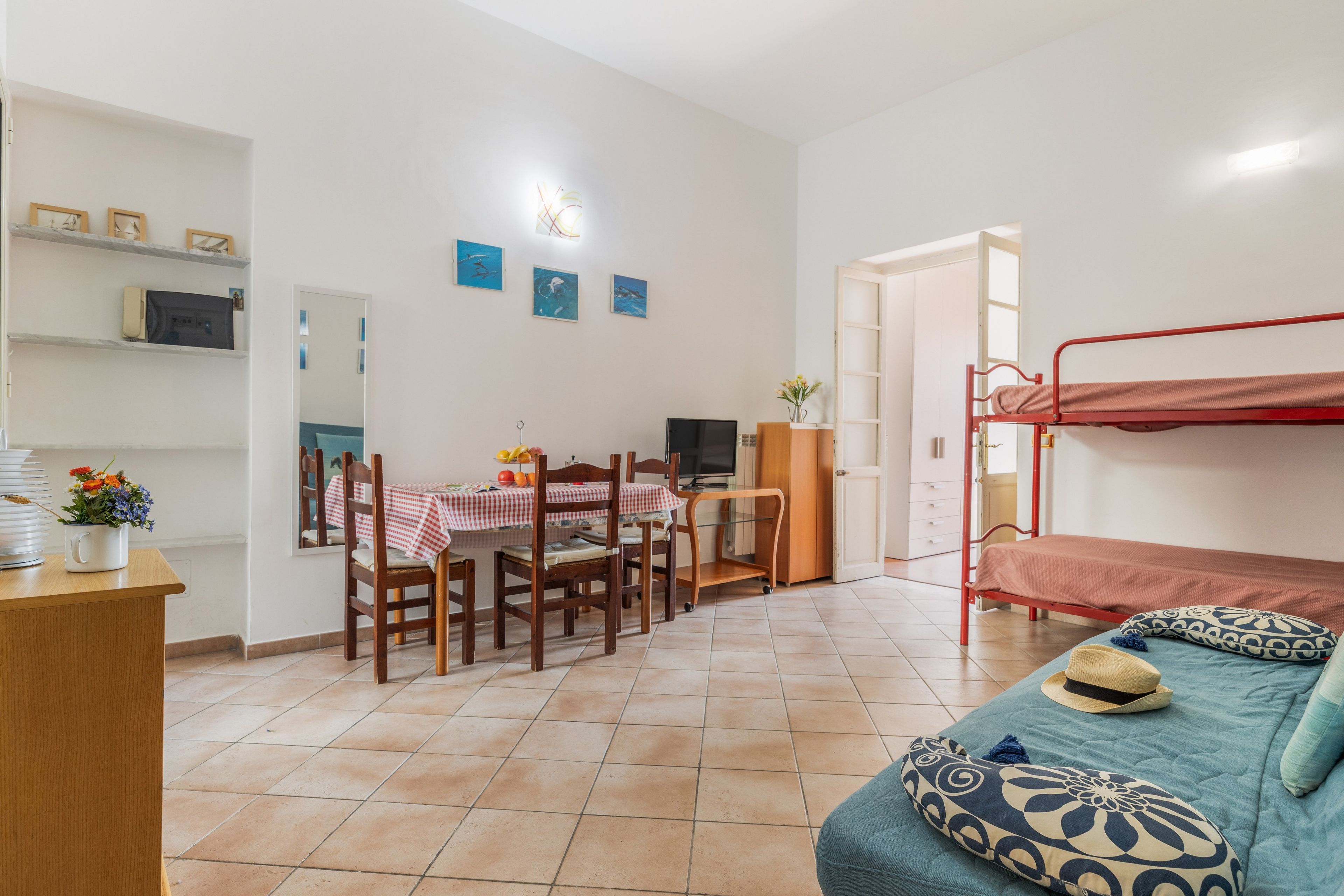 Ein kleines Zimmer mit Etagenbett, Esstisch mit Stühlen, kleinem Schreibtisch und Fernseher.