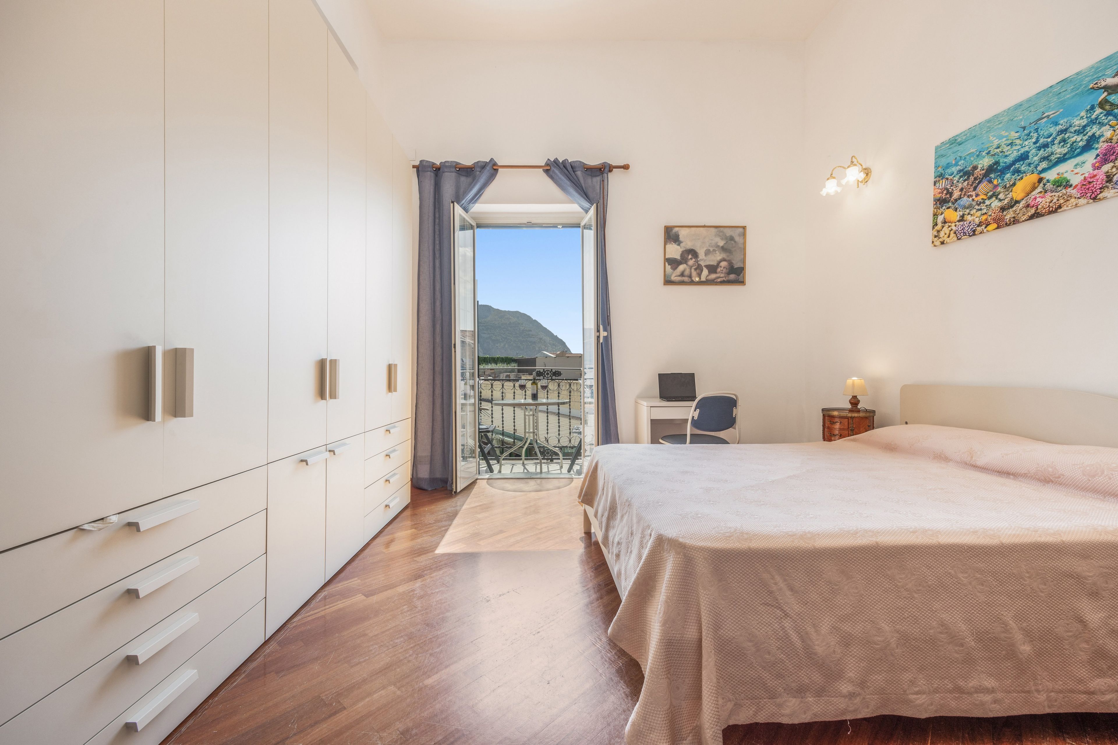 Une chambre à coucher avec un lit, un bureau et une chaise. Elle possède un balcon d’où l’on peut admirer le ciel et les montagnes.