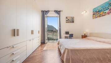 Une chambre à coucher avec un lit, un bureau et une chaise. Elle possède un balcon d’où l’on peut admirer le ciel et les montagnes.