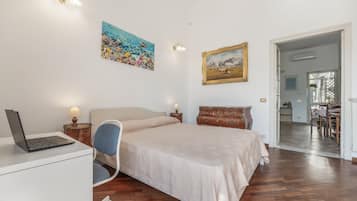 Een slaapkamer met een bed, een bureau met een laptop, een stoel, een kaptafel en twee schilderijen aan de muur.