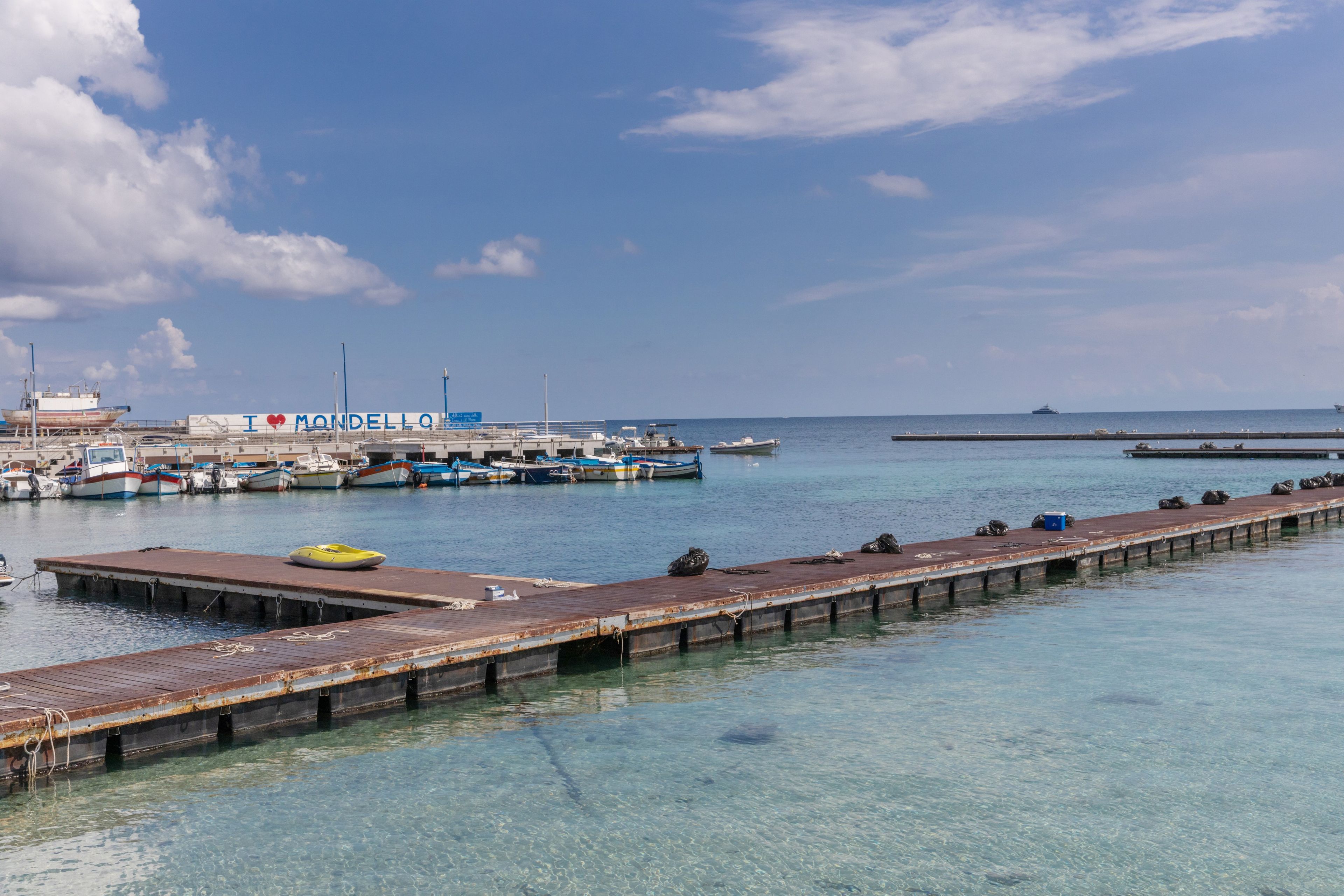 Een jachthaven met aangemeerde boten, een steiger die het water in loopt en een heldere lucht.