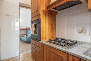 A kitchen with wooden cabinets, a gas stove, and a microwave. - Mondello Holidays - Casa Goethe Apartment with Sea View, WiFi, and Air Conditioning (Palermo)