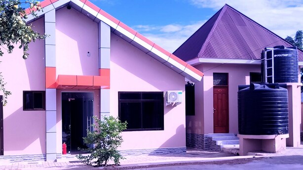 A two-story building with a pink facade and a red roof, featuring a water tank on the right side.