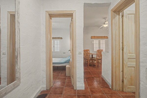 A hallway with a bed, a dining area, and a door.
