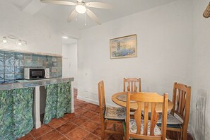 Un coin repas avec une table et des chaises en bois, un ventilateur de plafond, un four à micro-ondes et un pare-feu en carreaux.