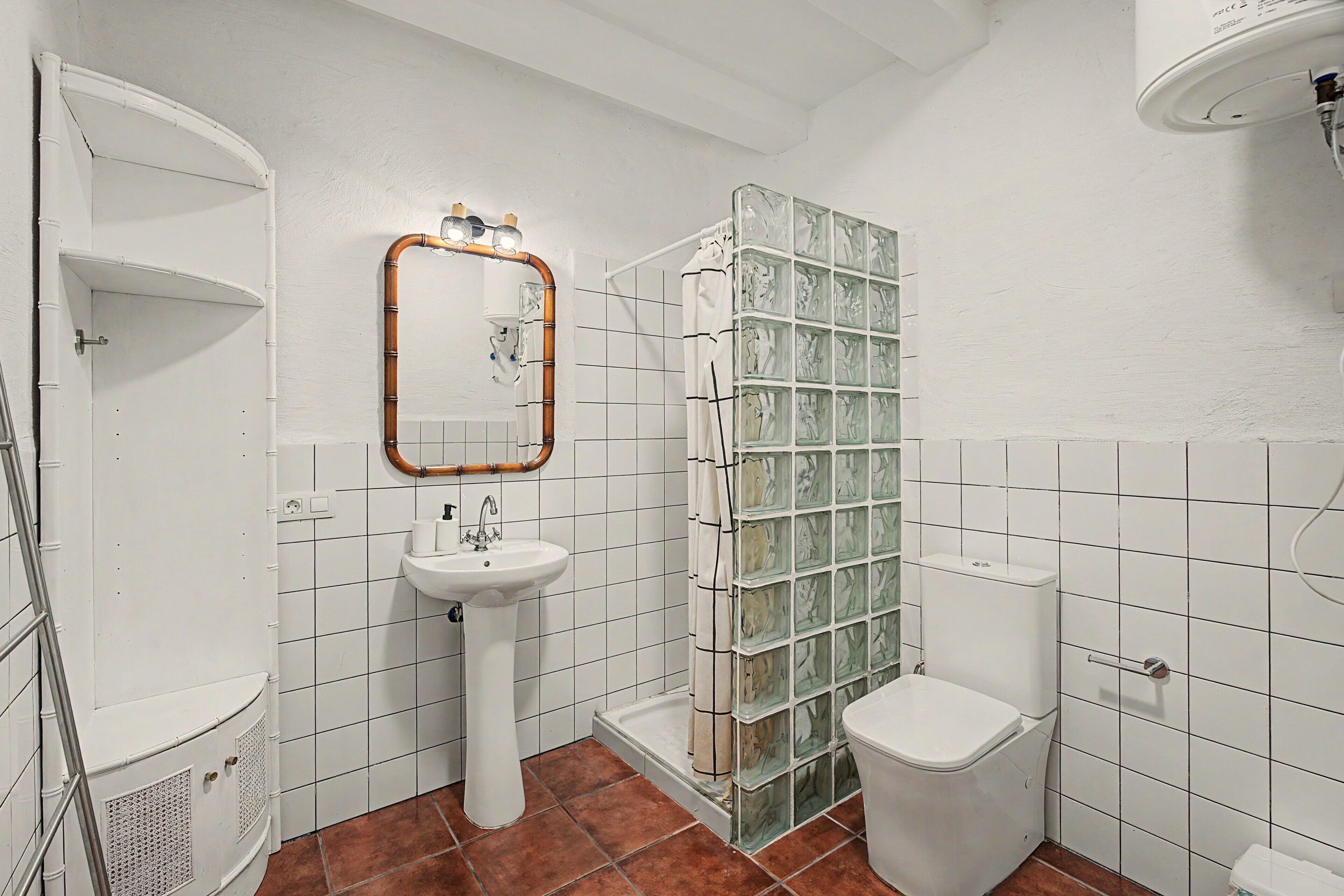 Et badeværelse med hvid vask, spejl, glasbrusekabine og toilet.