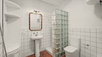 Et badeværelse med hvid vask, spejl, glasbrusekabine og toilet.