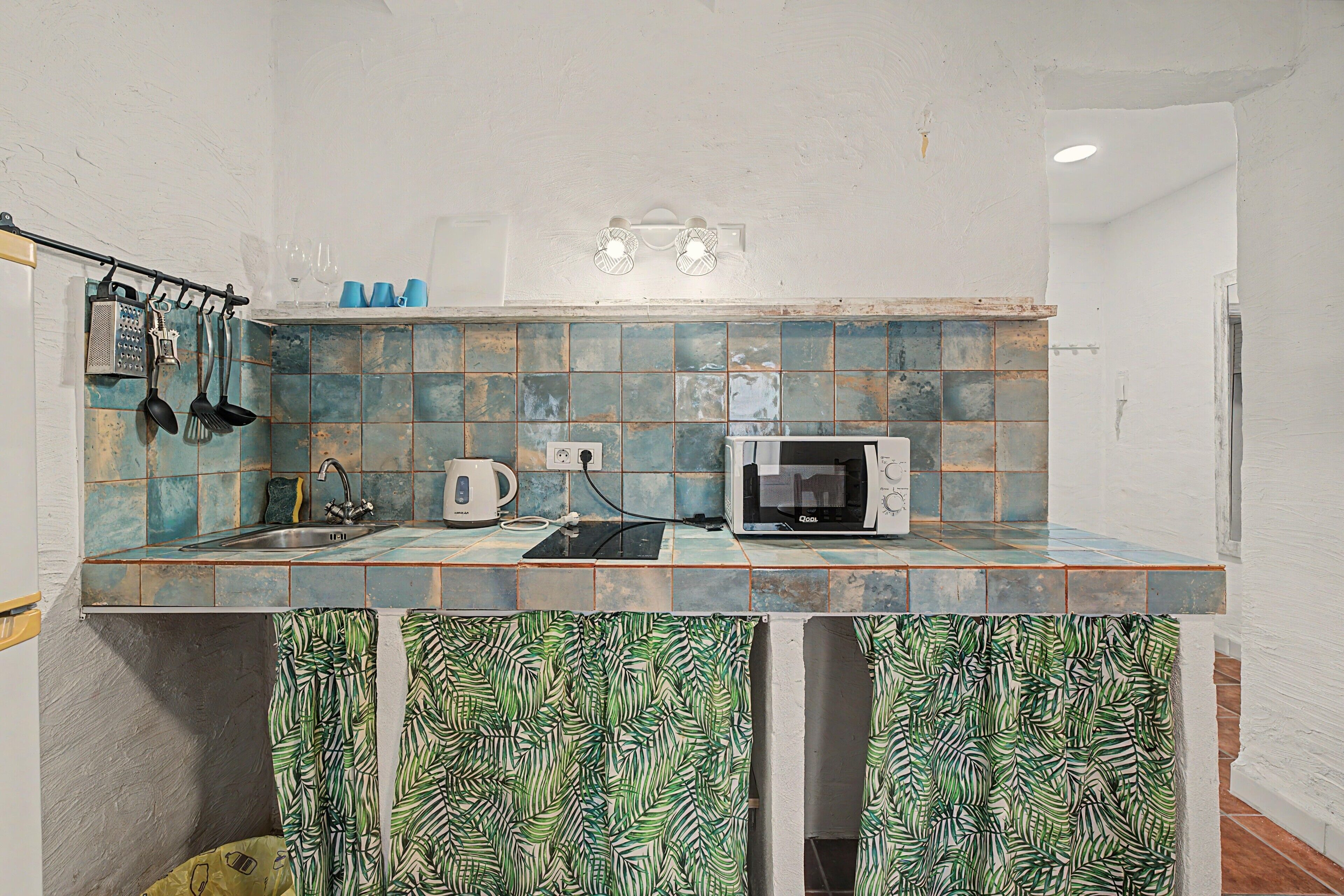 Una cocina con microondas, hervidor y utensilios en la encimera.
