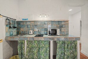 A kitchen with a microwave, kettle, and utensils on the counter.
