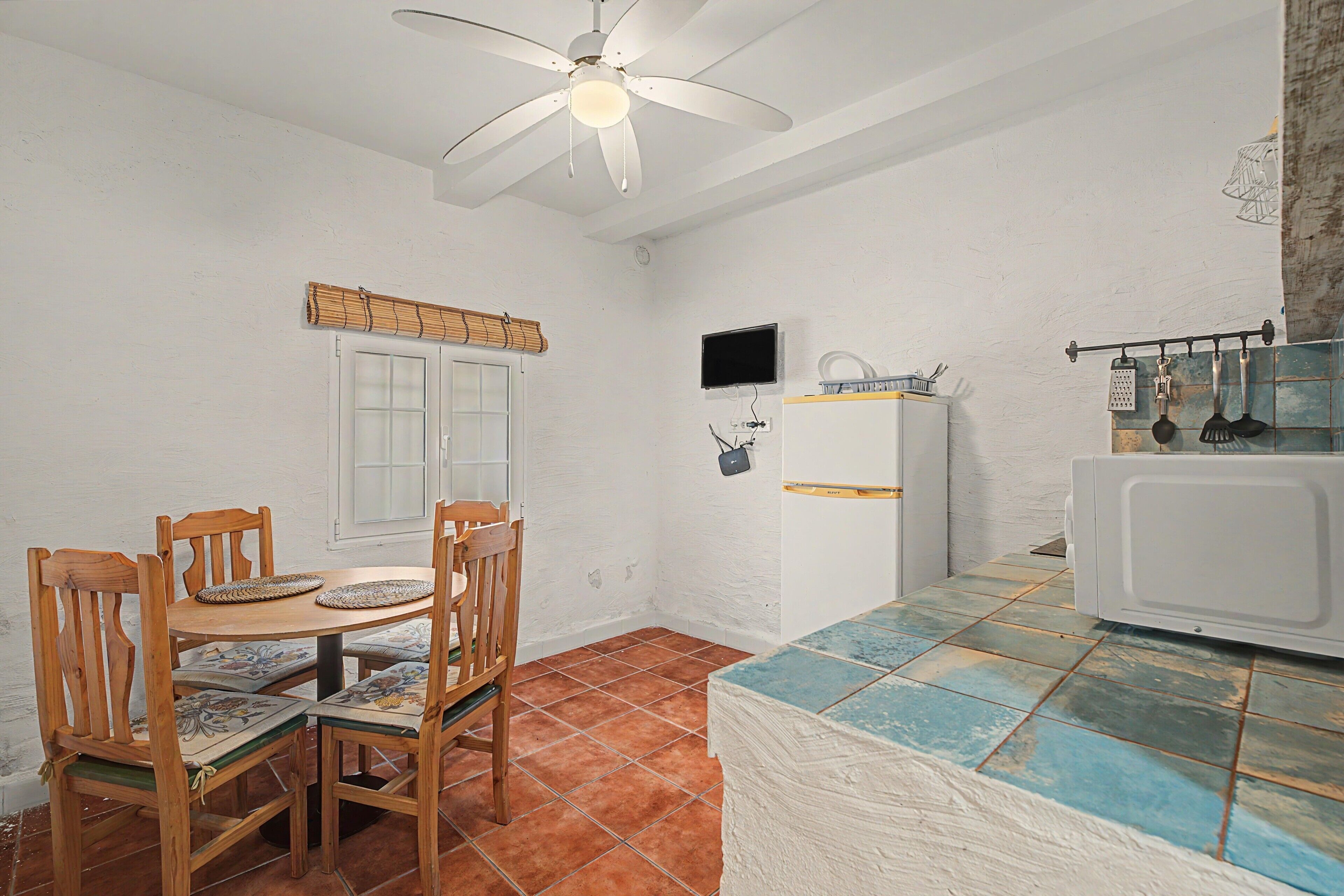 Una cocina con una mesa de comedor, sillas, ventilador de techo, refrigerador y salpicadero de azulejos.