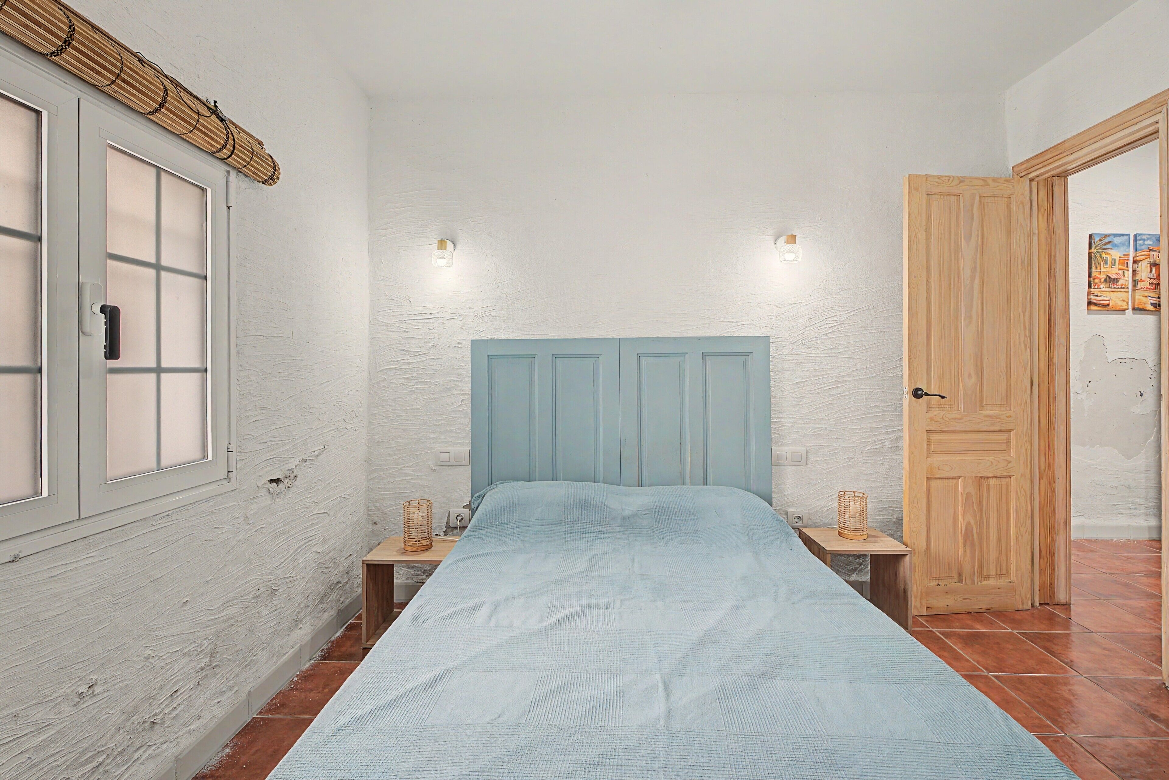 Una habitación pequeña con cama, ventana y puerta.