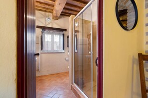 Un pasillo con una puerta de vidrio que da a un baño, un radiador y una ventana con cortinas.