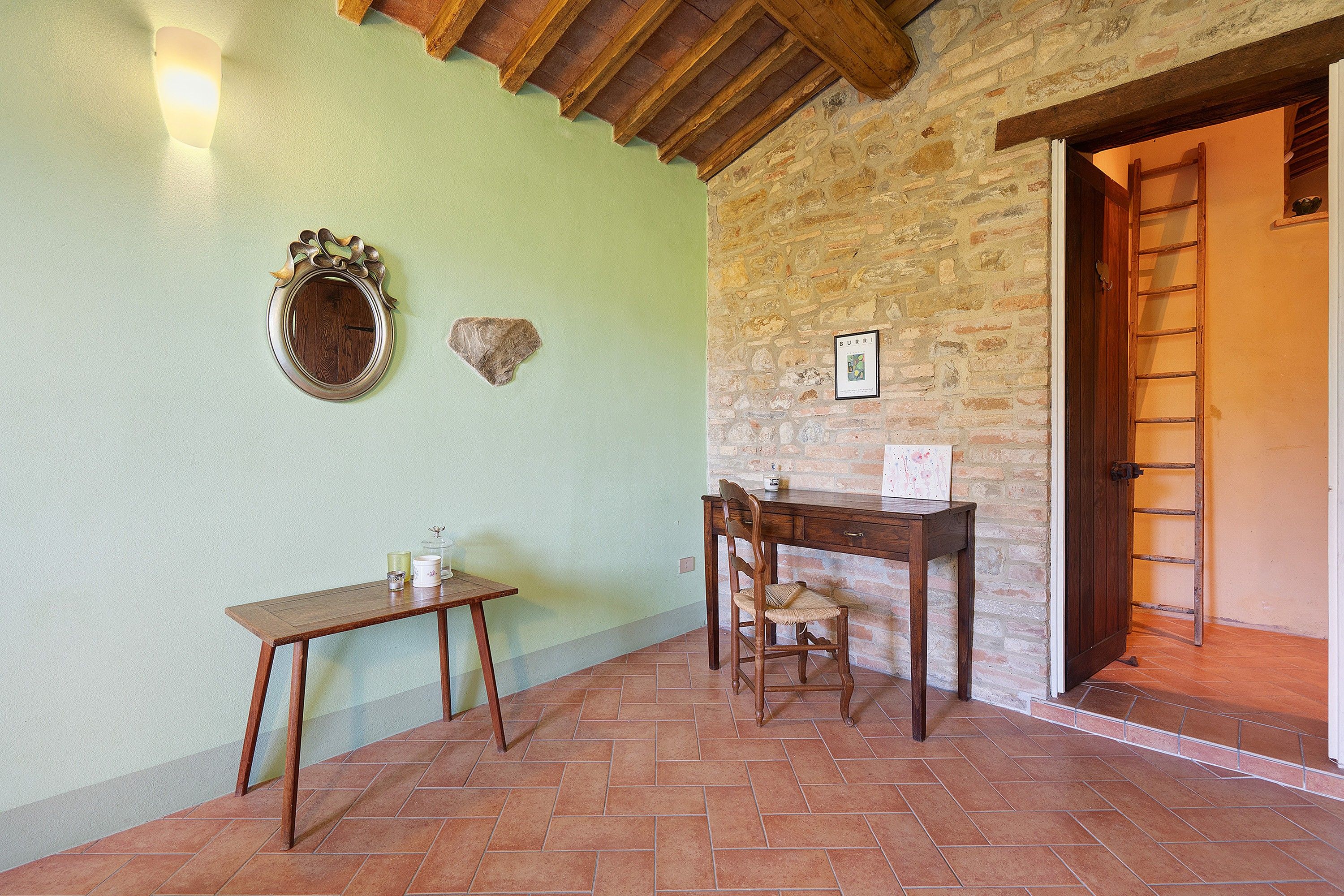 Une pièce rustique avec une table en bois, une chaise, une petite table d’appoint, un miroir fixé au mur et un mur en pierre.