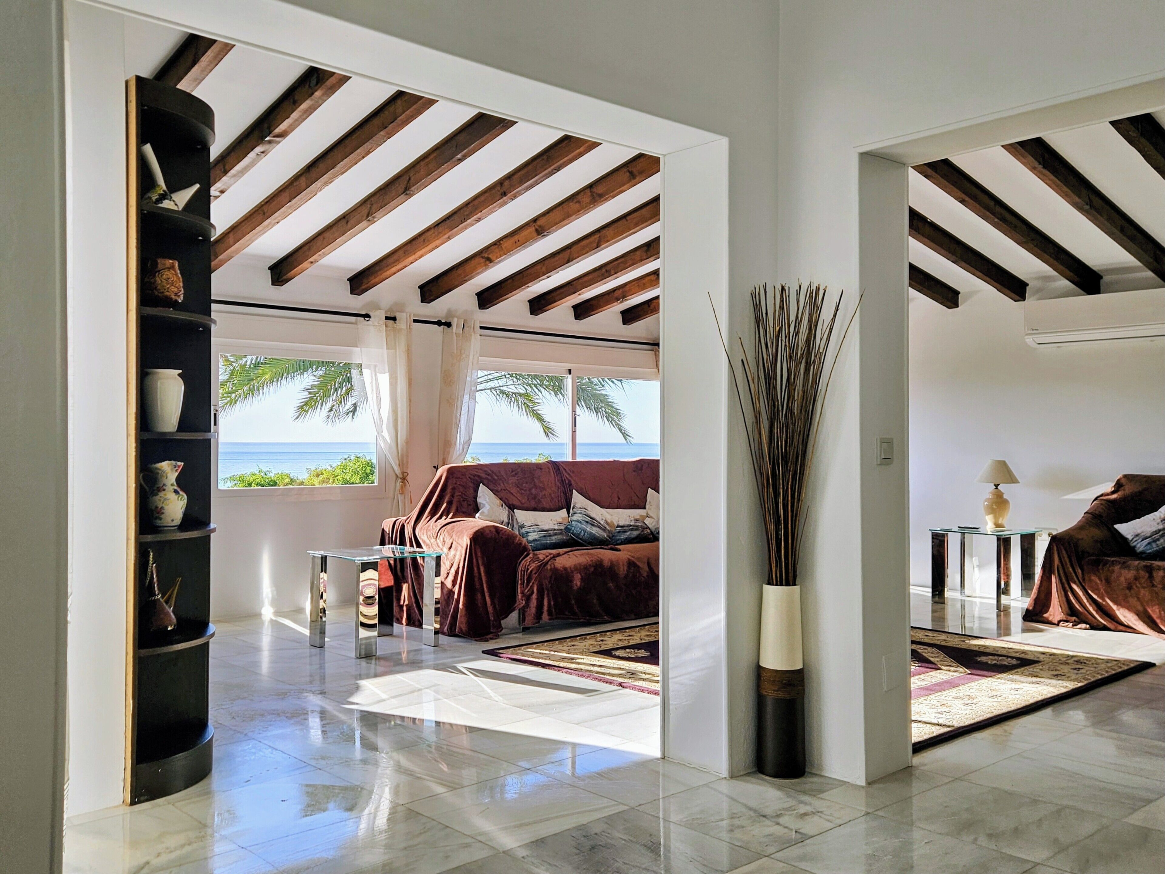 A spacious room with a large window overlooking the sea, a cozy seating area with a sofa and a coffee table, and a decorative vase on a shelf.