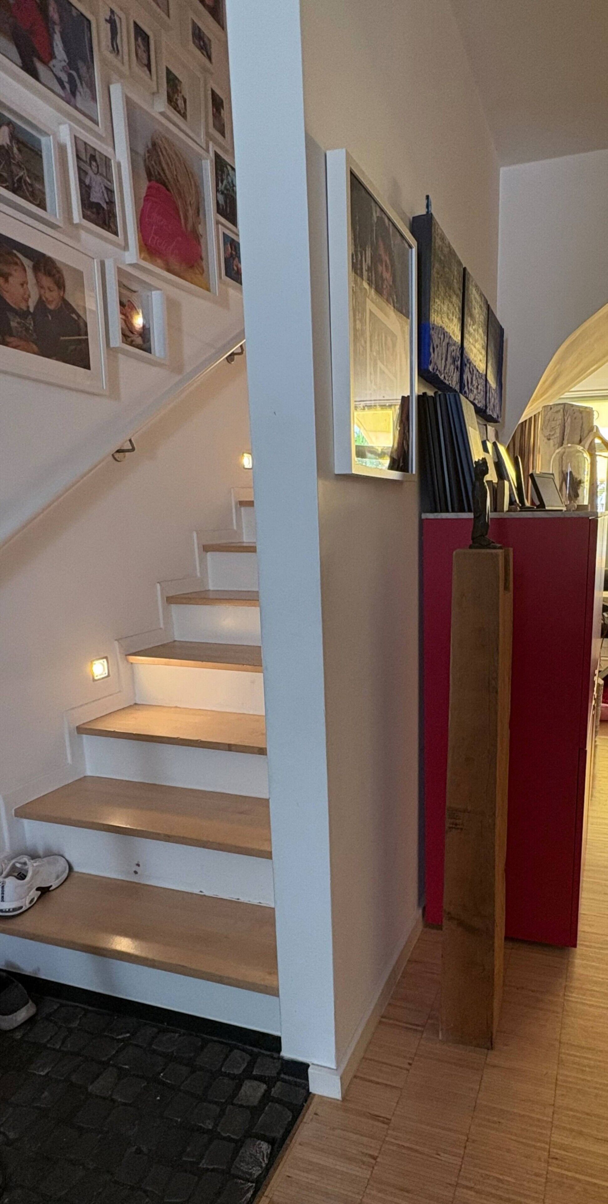 Eine Treppe mit Handlauf, die zu einer Zwischenebene mit einem roten Schrank und verschiedenen ausgestellten Gegenständen führt.