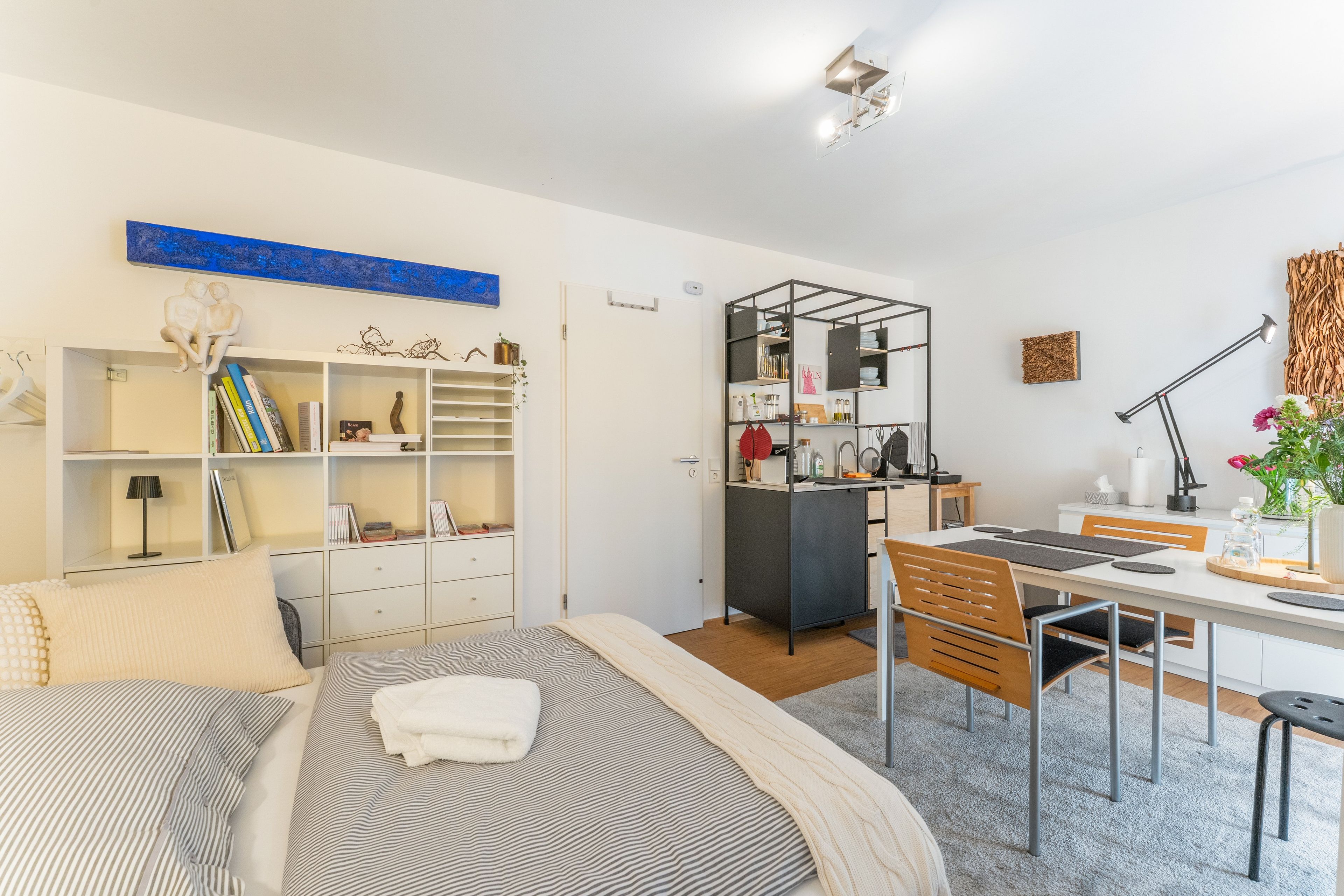 A modern, well-lit room with a bed, a desk, and a dining area.