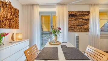 Un espace repas moderne avec une table blanche, des sets de table gris, des chaises en bois et un vase rempli de fleurs.
