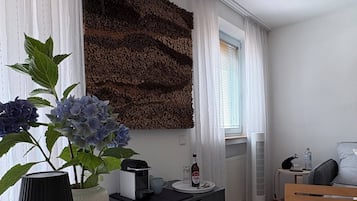 Ein modernes Zimmer mit einem weißen Tisch, einer Wanddekoration, einer Topfpflanze und einem Nachttisch mit einer Lampe.