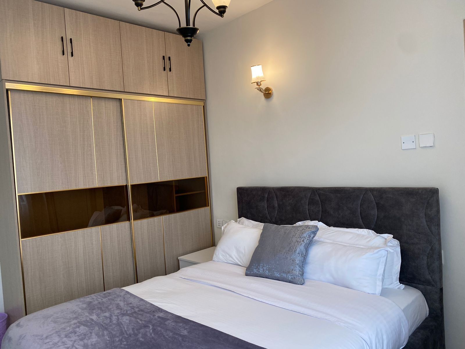 A bedroom with a bed, a wardrobe, and a wall-mounted light fixture.