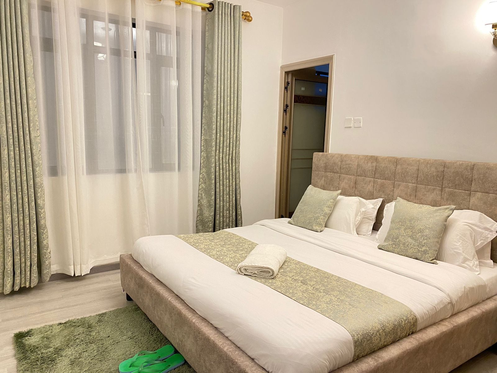 Quarto de hotel com cama, cortinas, uma porta e um tapete pequeno.