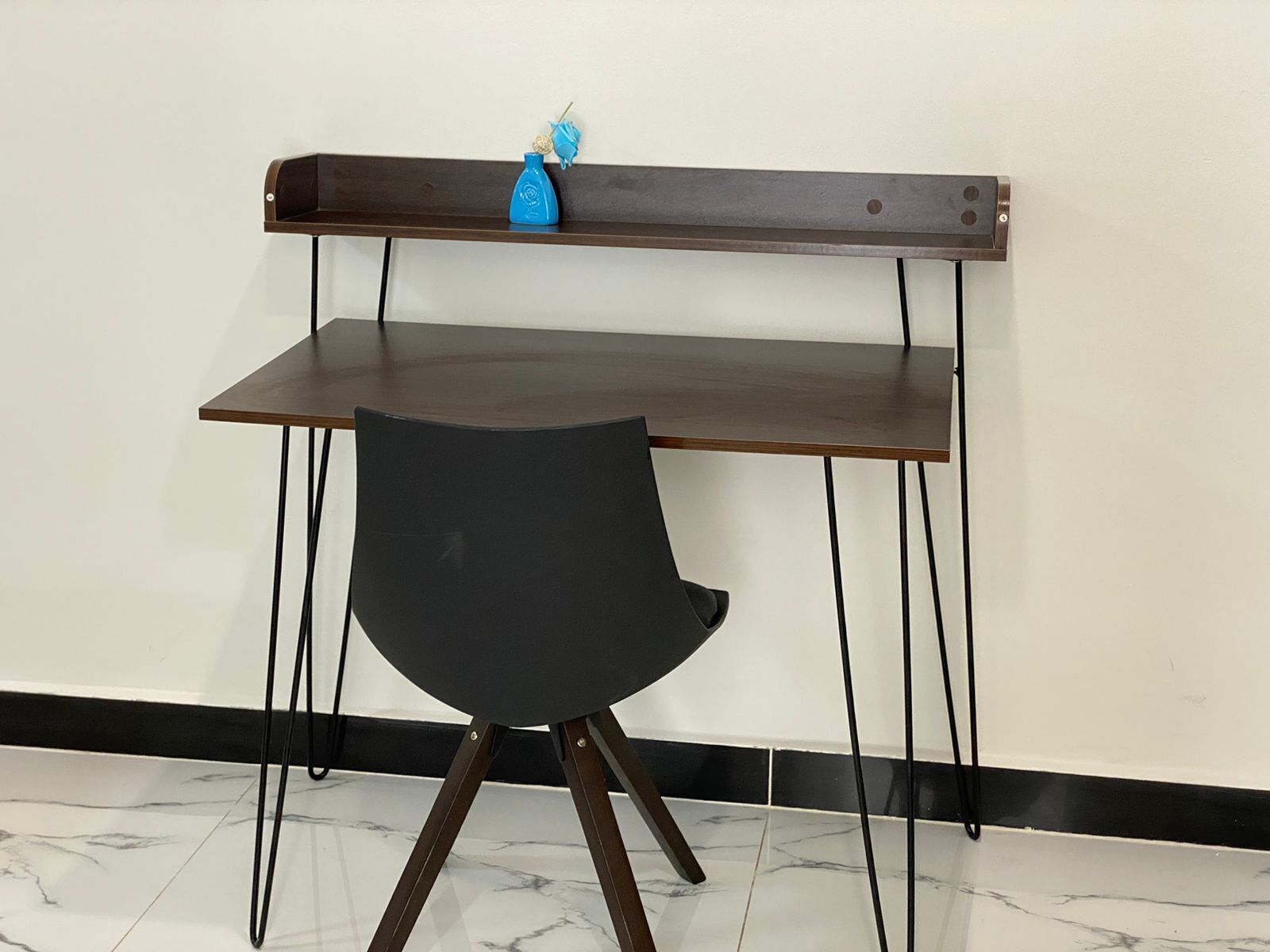 A desk with a chair, a blue vase, and a wall-mounted shelf.