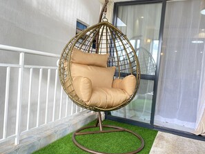 Uma cadeira suspensa com almofadas, um corrimão branco e uma porta de vidro ao fundo.