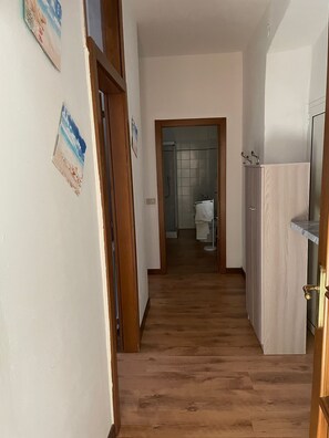 Un pasillo con piso de madera que conduce a un baño con puerta de vidrio.