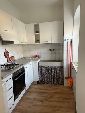 A compact kitchen with white cabinets, a gas stove, a built-in oven, and a patterned curtain. - CASA ZANONI (Nago-Torbole)