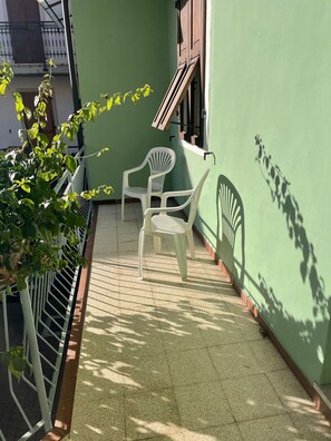 A small outdoor area with a green wall, two white plastic chairs, and a potted plant. - CASA ZANONI (Nago-Torbole)