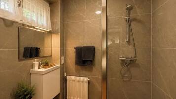 A bathroom with a shower, a mirror, a towel rack, and a radiator.