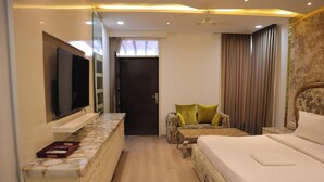 Habitación de hotel con cama, televisor montado en la pared, zona de estar con cojines y puerta que da a otra habitación.