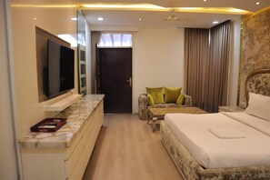 Habitación de hotel con cama, televisor montado en la pared, zona de estar con cojines y puerta que da a otra habitación.