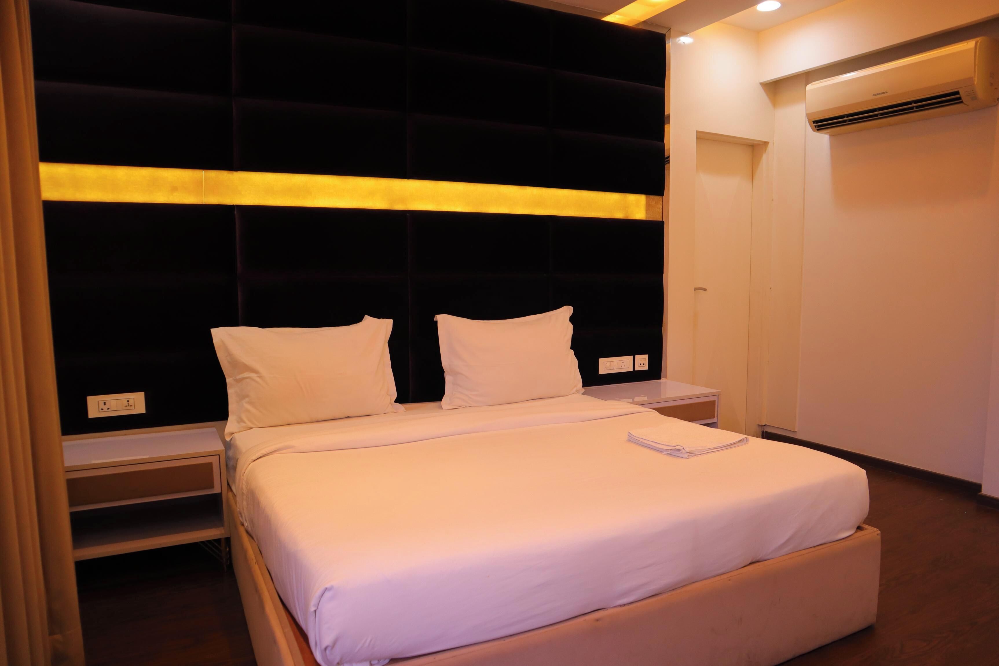 A modern bedroom with a large bed, a headboard with a light strip, a bedside table, and an air conditioning unit.