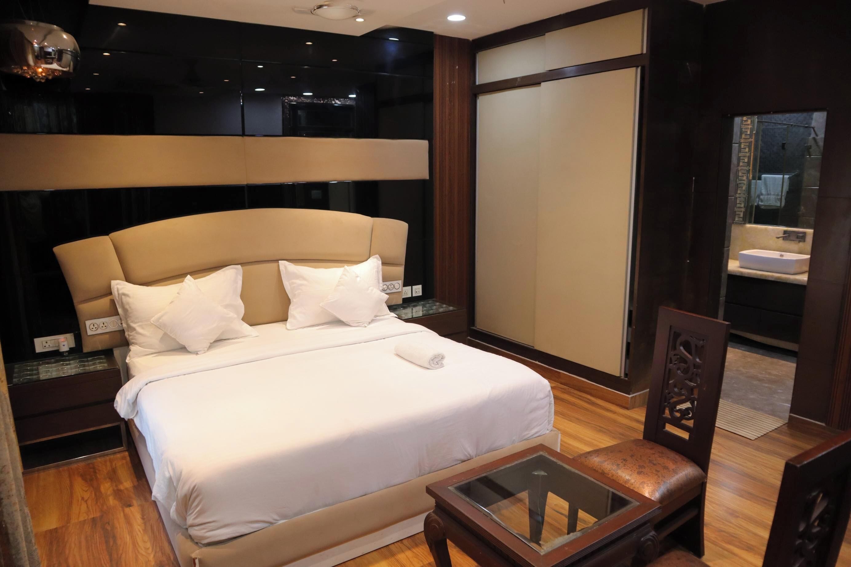 Habitación de hotel con una cama grande, una mesa con superficie de vidrio y vistas a la ciudad a través de un ventanal amplio.