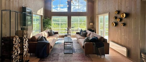 A spacious living room with a high ceiling, large windows, and a central coffee table.