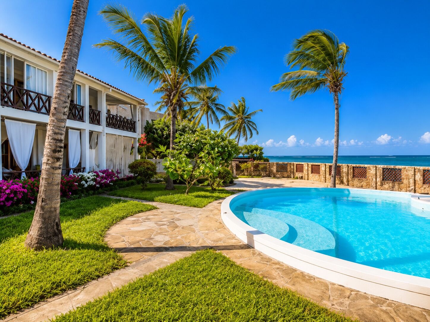 A poolside view with a clear blue sky, palm trees, and a building with a balcony.
