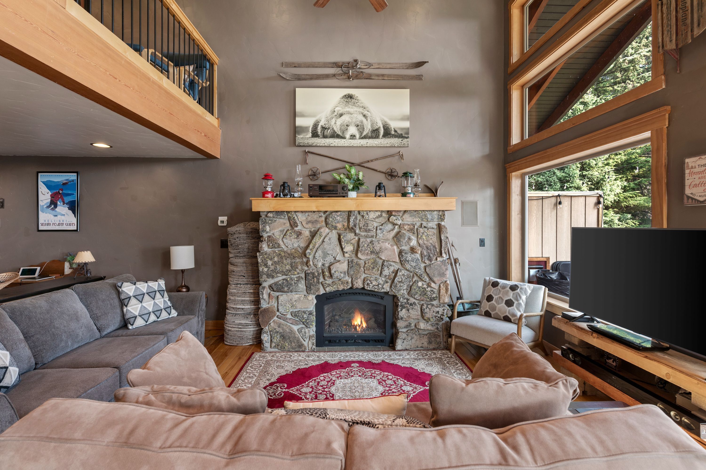 A cozy living room with a stone fireplace, a comfortable sofa, a television, and a large window offering a view of the outdoors.