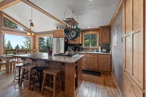A spacious kitchen with a large island, wooden cabinets, and a view of the outdoors. - Snowplow Home | Hot Tub + Dog Friendly (Sandpoint)