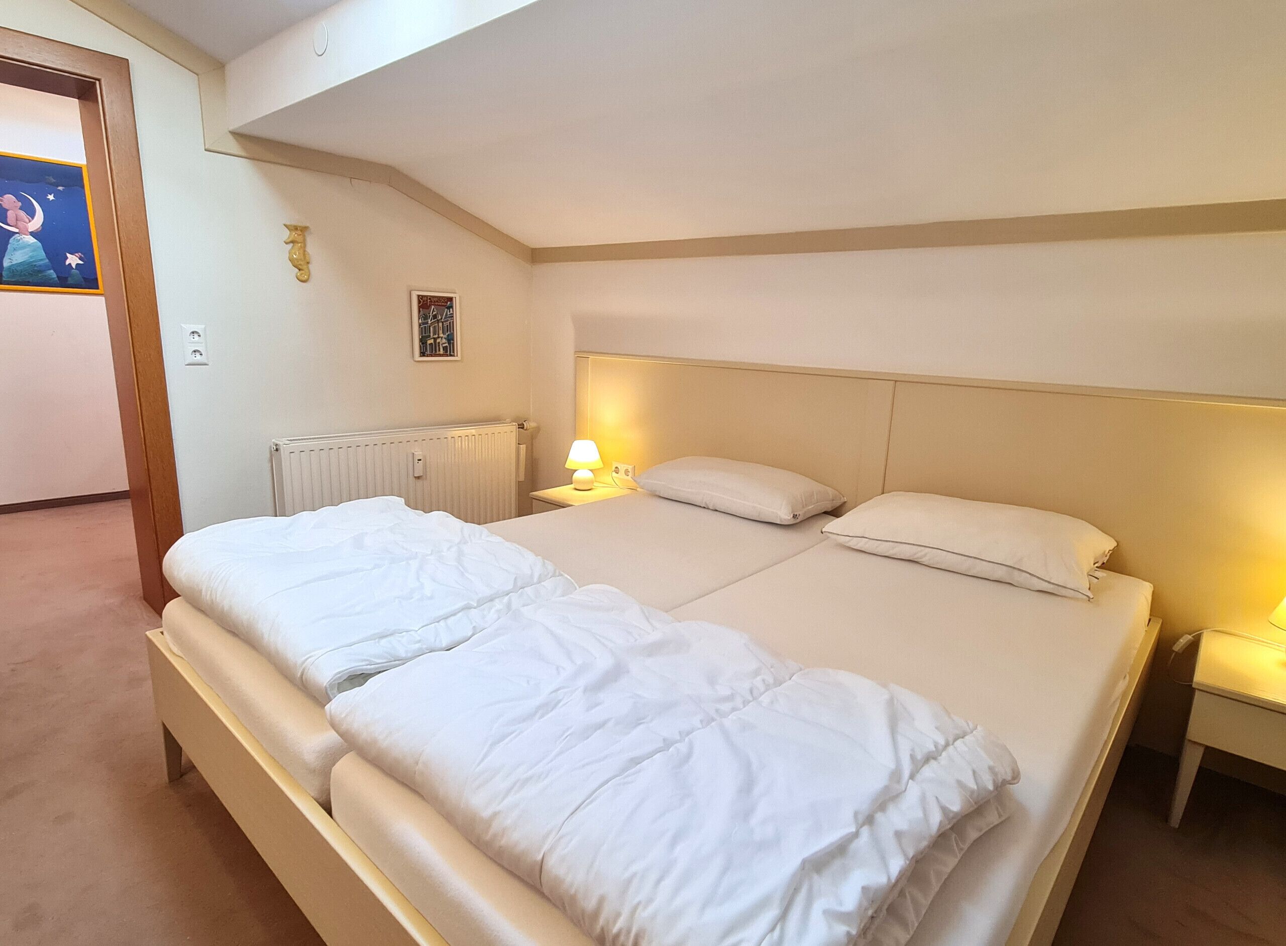 Een tweepersoonsbed met hoofdeinde, een bedlampje en een wanddecoratie.