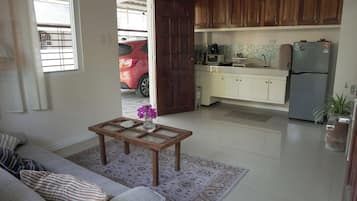 Una sala de estar con sofá, una mesa de centro con un jarrón, y una cocina con alacenas de madera y electrodomésticos.