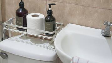 Une salle de bain équipée de toilettes, d’un lavabo et d’une étagère où sont rangés les articles de toilette.