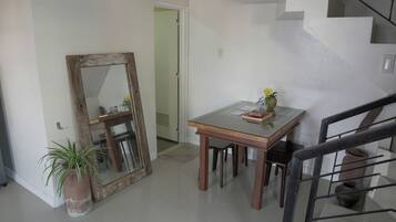 Una habitación con una mesa de comedor, sillas, un espejo grande, una planta en maceta y una escalera.