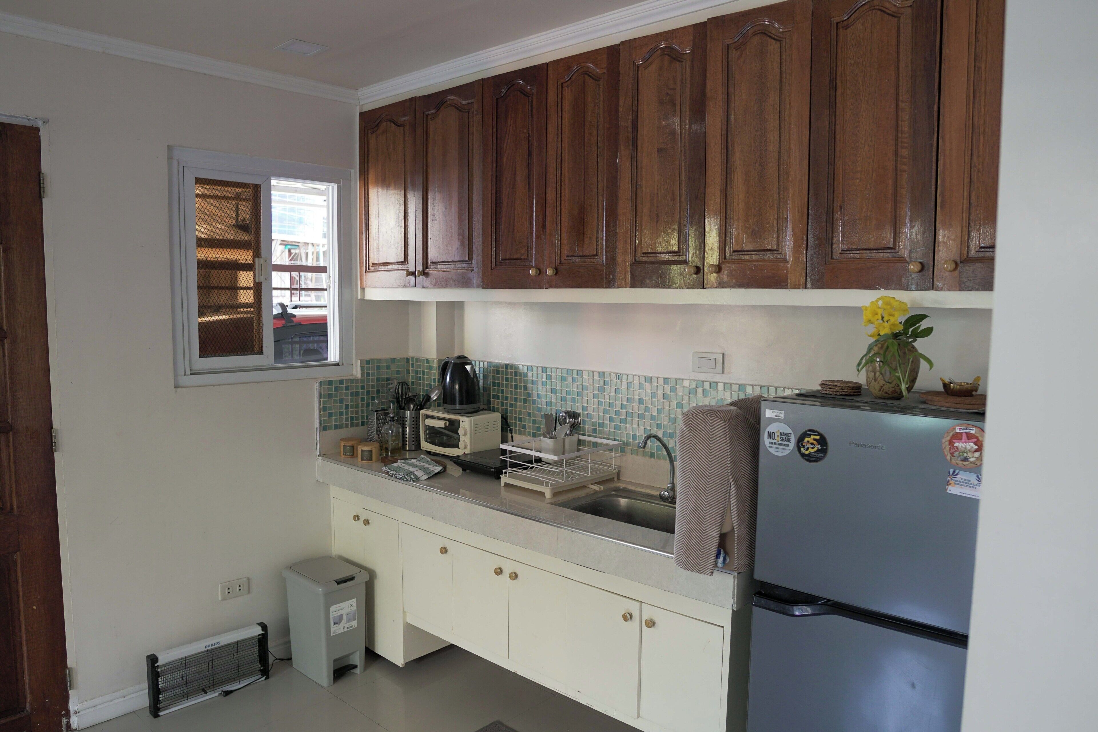 A kitchen with wooden cabinets, a built-in microwave, a refrigerator, and a window with a view of the outside.