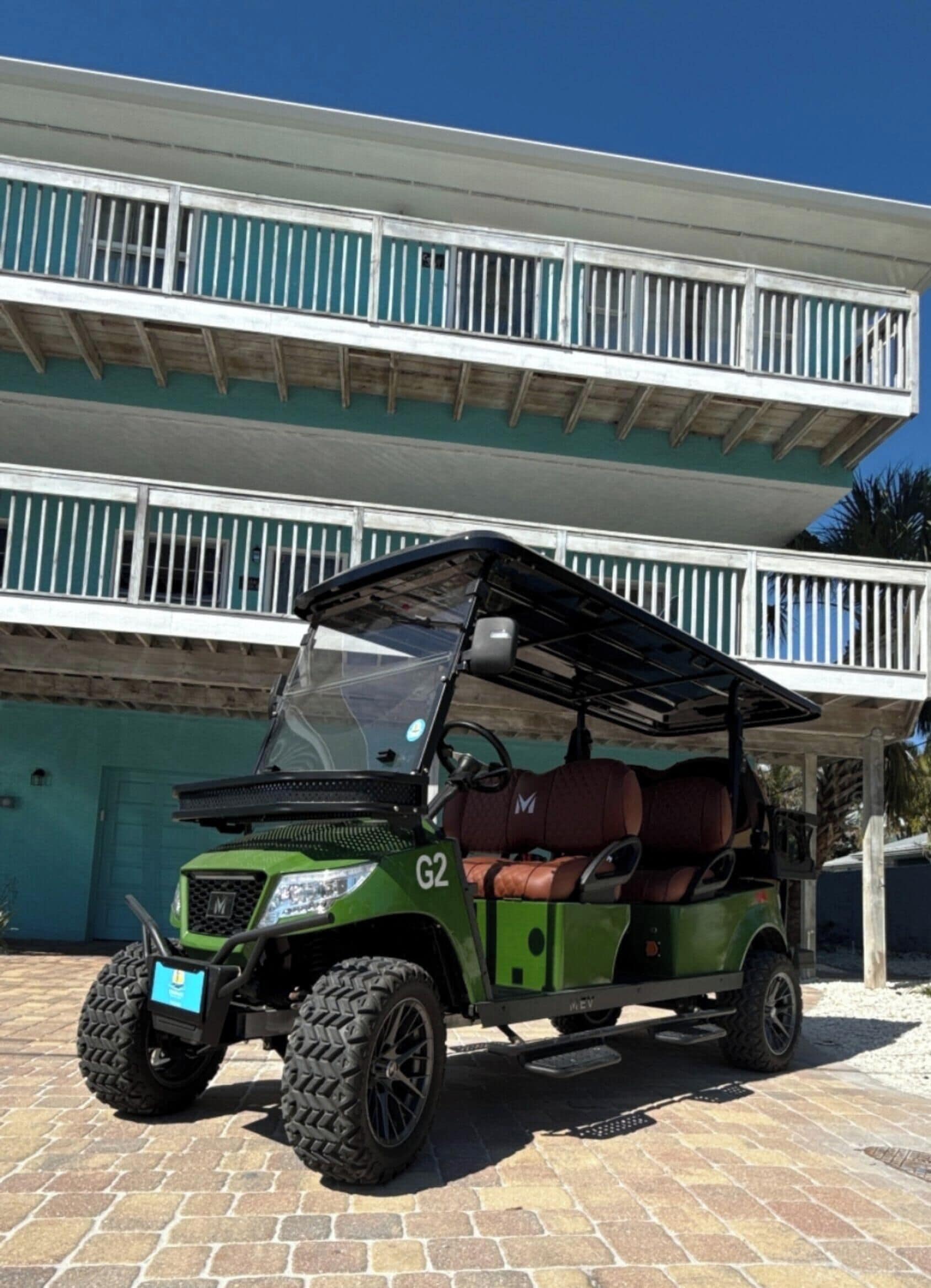Un véhicule utilitaire vert est garé devant un immeuble à deux étages doté d’un balcon.