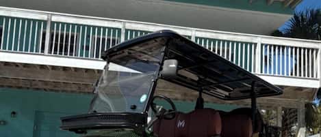 A green utility vehicle parked in front of a two-story building with a balcony.