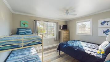 A bedroom with two bunk beds, a ceiling fan, a dresser, and artwork on the walls.